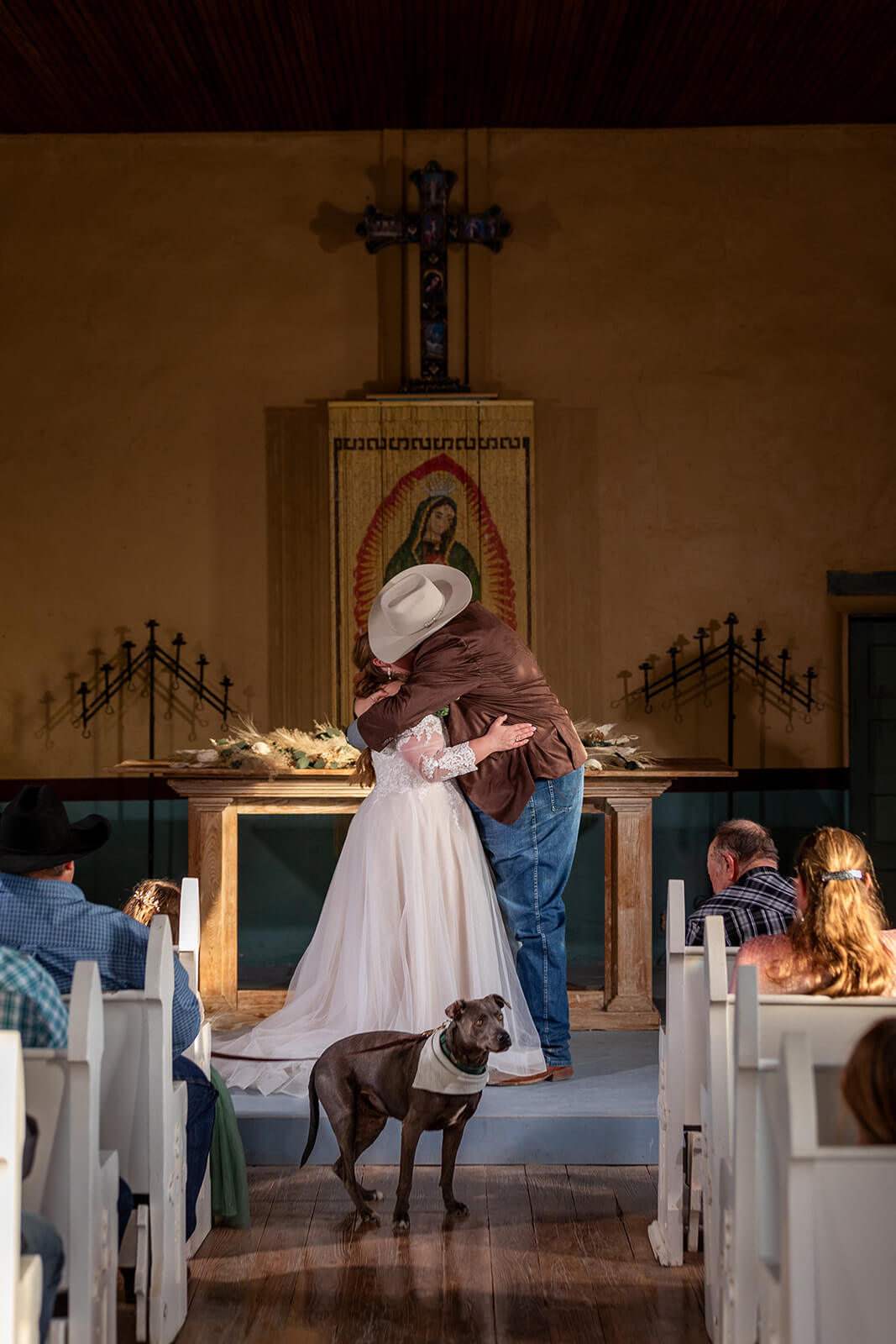 The First Kiss as Mr and Mrs Couple sharing their first kiss inside Saint Agnes Church in Terlingua TX with their friends, family, and pup cheering them on.